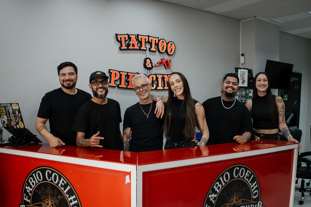 The Fábio Coelho Tattoo & Piercing team behind the studio's red reception counter